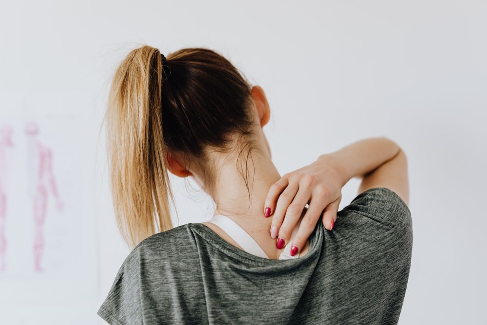 Woman easing neck and shoulder pain — a common reason families book home physiotherapy